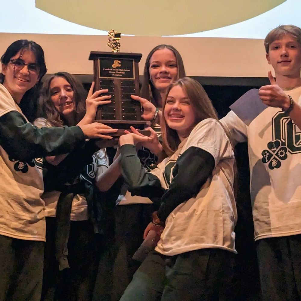 8th grade students wearing Camden Catholic t-shirts hold up a trophy after winning a STEM Challenge
